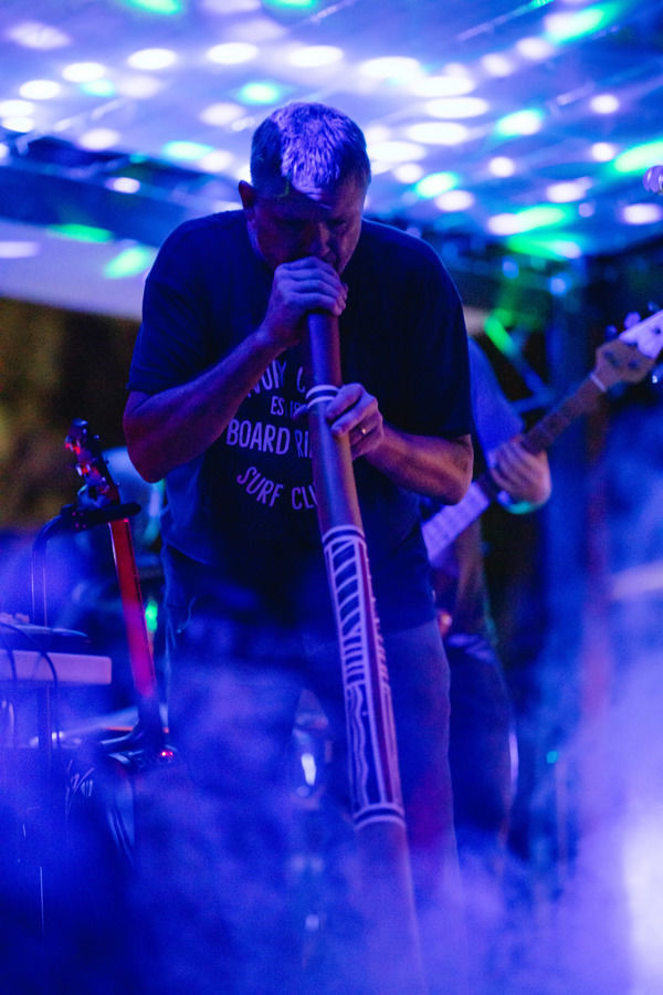 Man playing a didgeridoo on a stage with purple lights and background